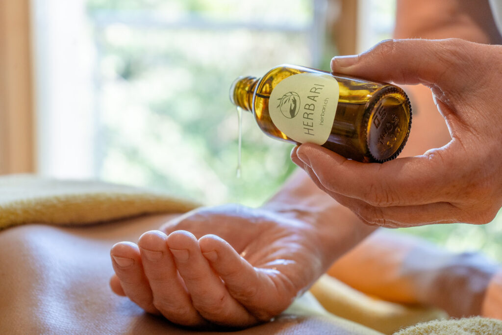 Massageöl wird aus einer kleinen Glasflasche in die Handfläche geleert.