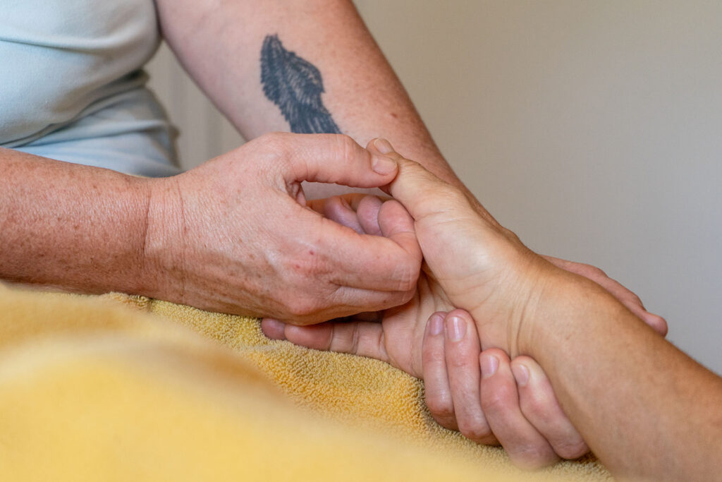 Hand der Masseurin hält die Hand einer Klientin und massiert sanft bin dem Daumen die Handseite.